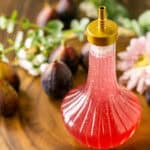 A bottle of fig simple syrup on a wooden serving platter with flowers and fresh figs scattered in the background.