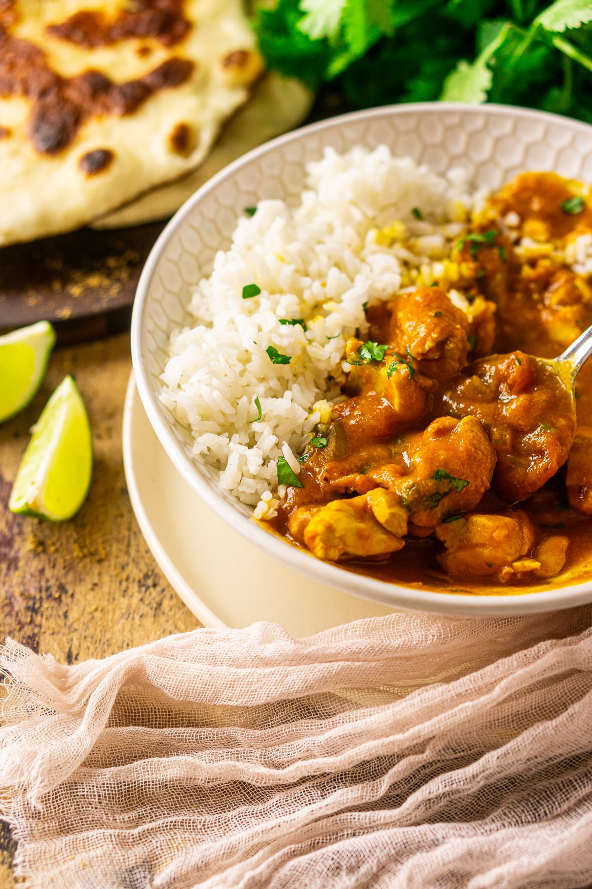 A spoon pulling up a scoop of the pumpkin and chicken curry in a cream-colored bowl.