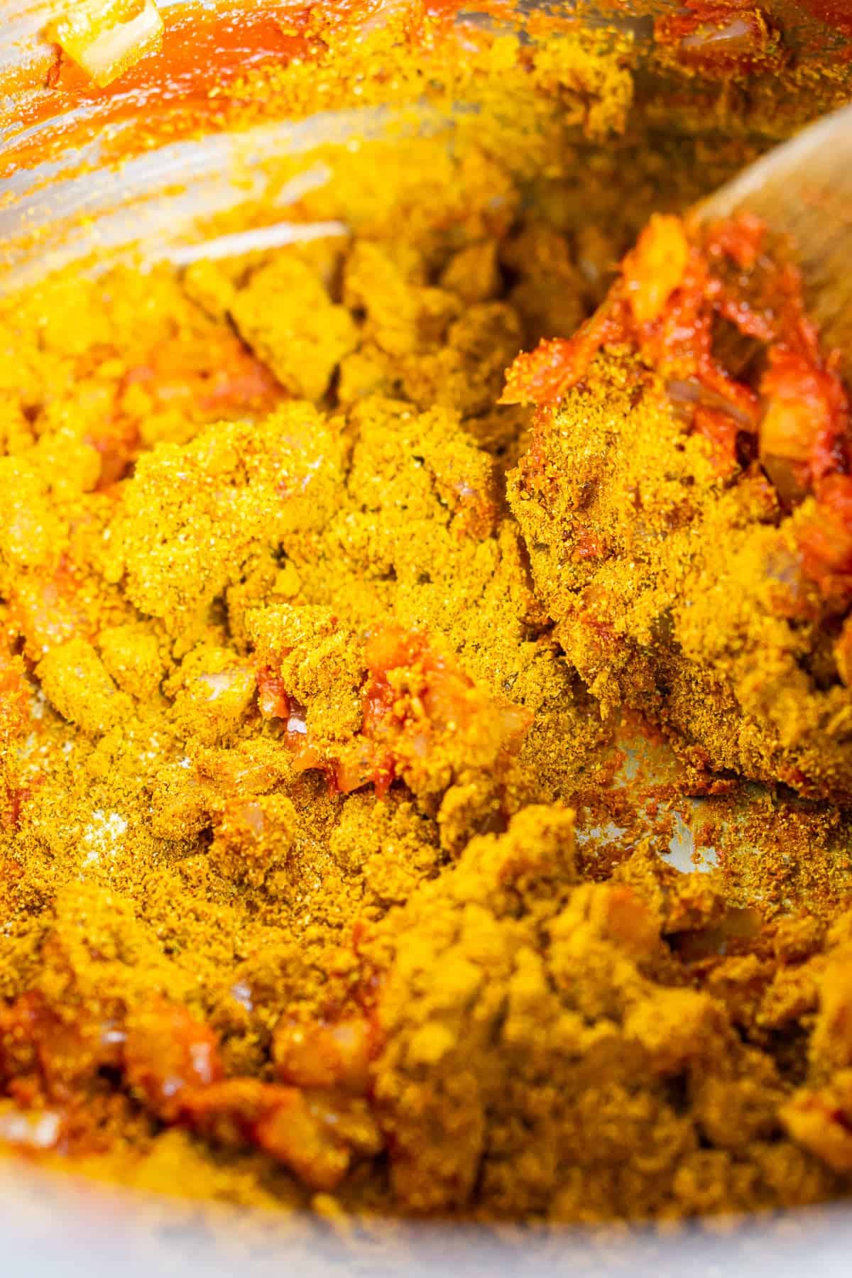 A brown spoon stirring the tomato paste and spices to bloom in a pot.