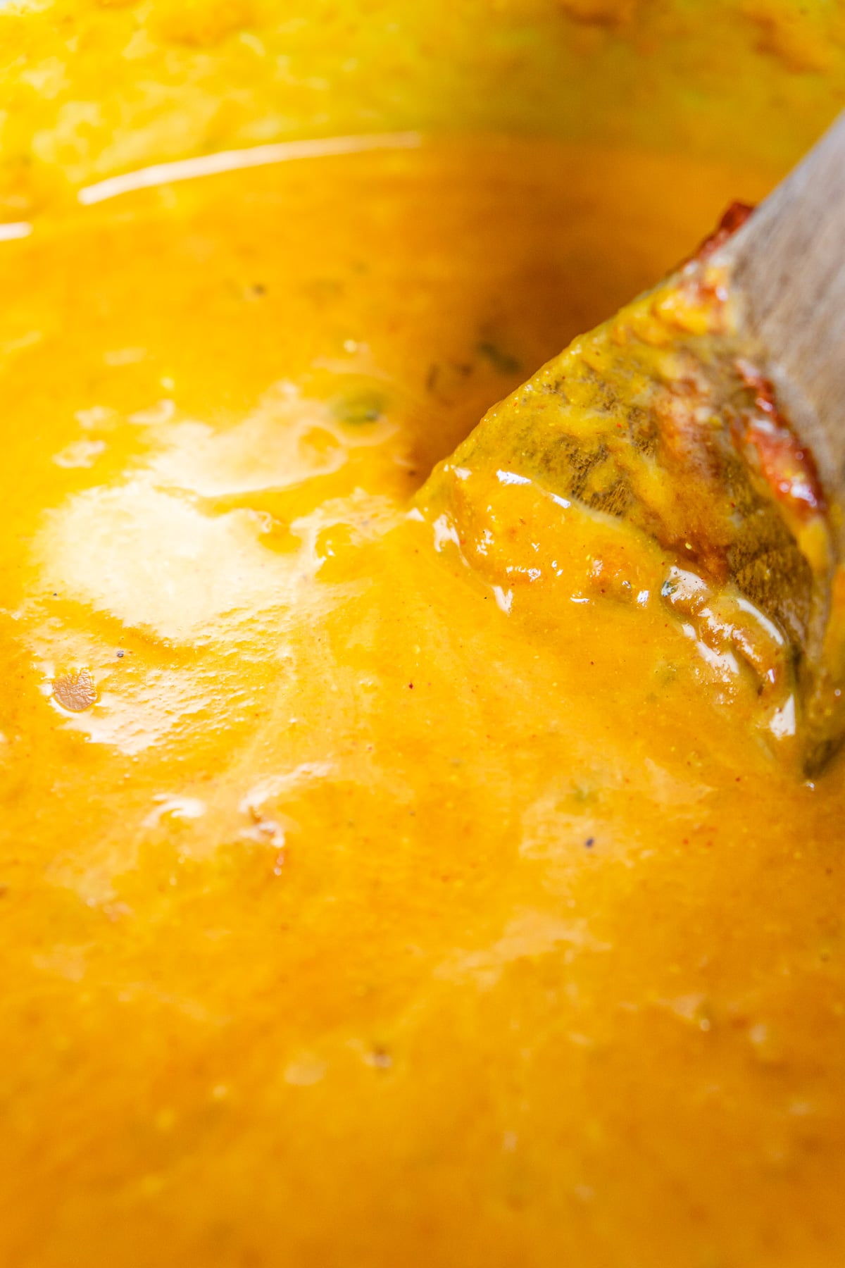 A brown wooden spoon stirring the pumpkin, chicken stock, and coconut milk into the curry.