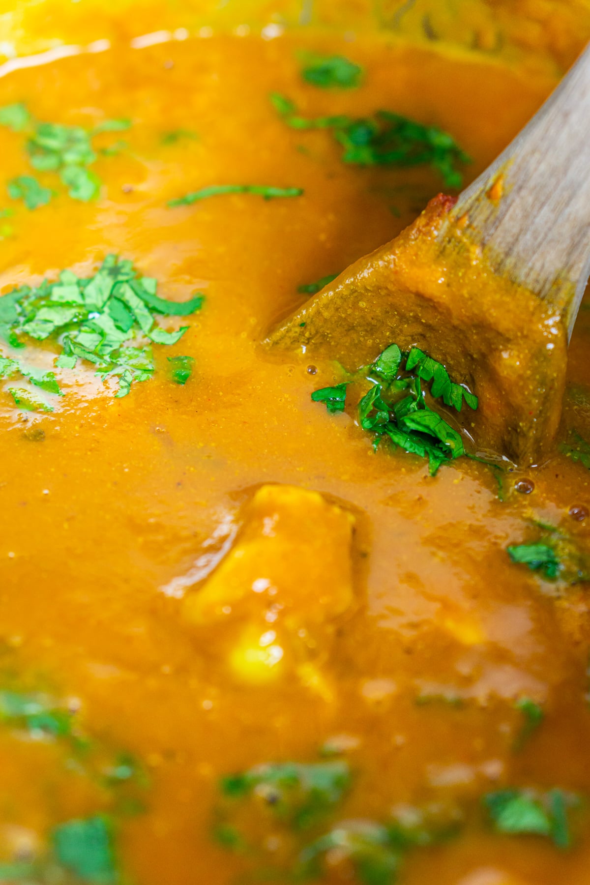 A brown wooden spoon stirring in chopped cilantro and lime juice into the curry after simmering.